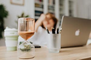 Sablier posé sur un bureau avec un ordinateur portable, symbolisant le temps qui passe et la procrastination