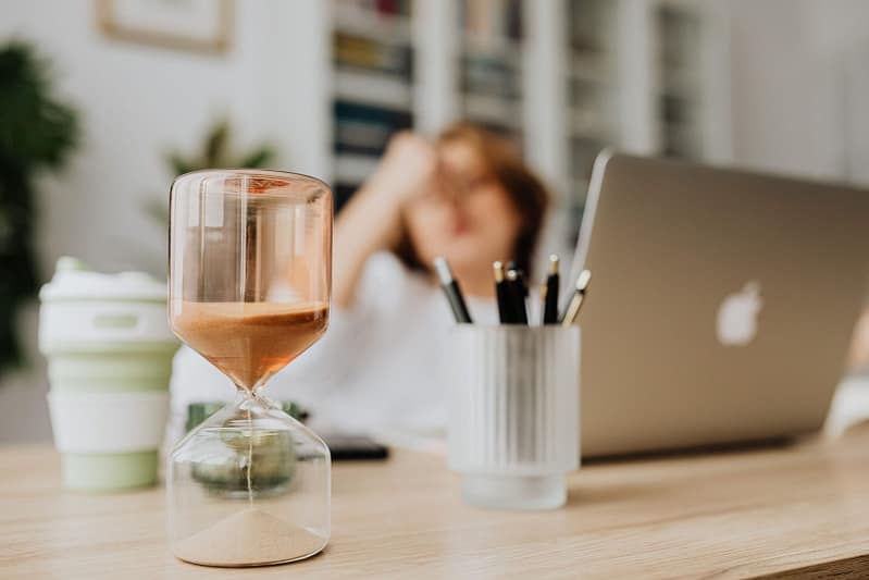 Sablier posé sur un bureau avec un ordinateur portable, symbolisant le temps qui passe et la procrastination
